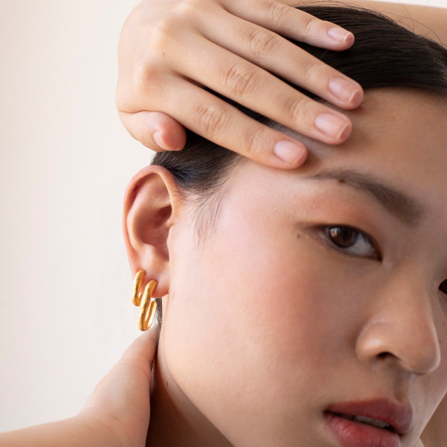Close-up of a person wearing a gold hoop earring with a neutral background