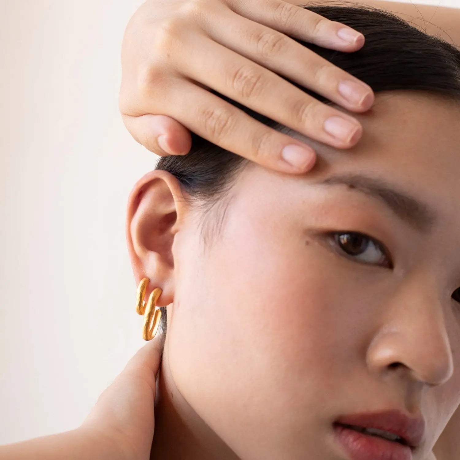 Close-up of a person wearing a gold hoop earring with a neutral background