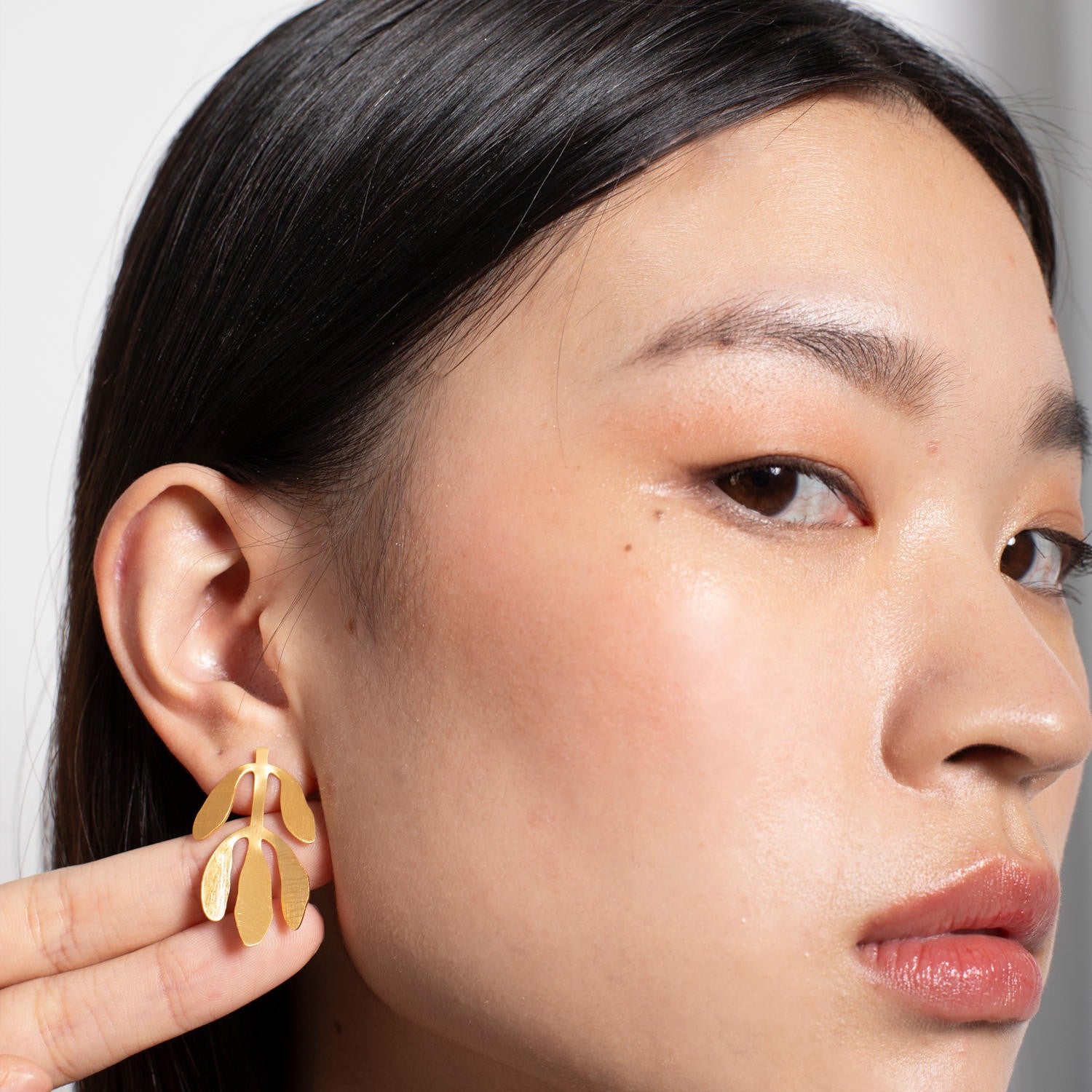 Close-up of a person wearing gold earrings with a neutral background
