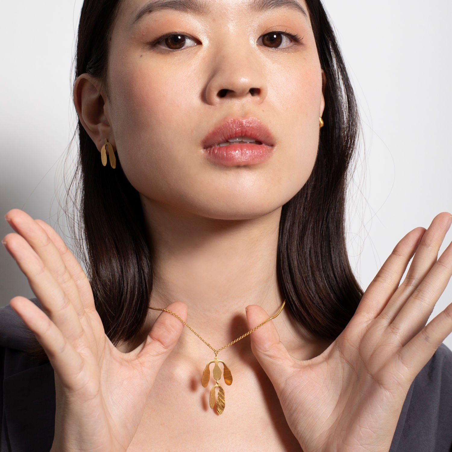 Woman wearing a gold necklace with a leaf pendant against a neutral background