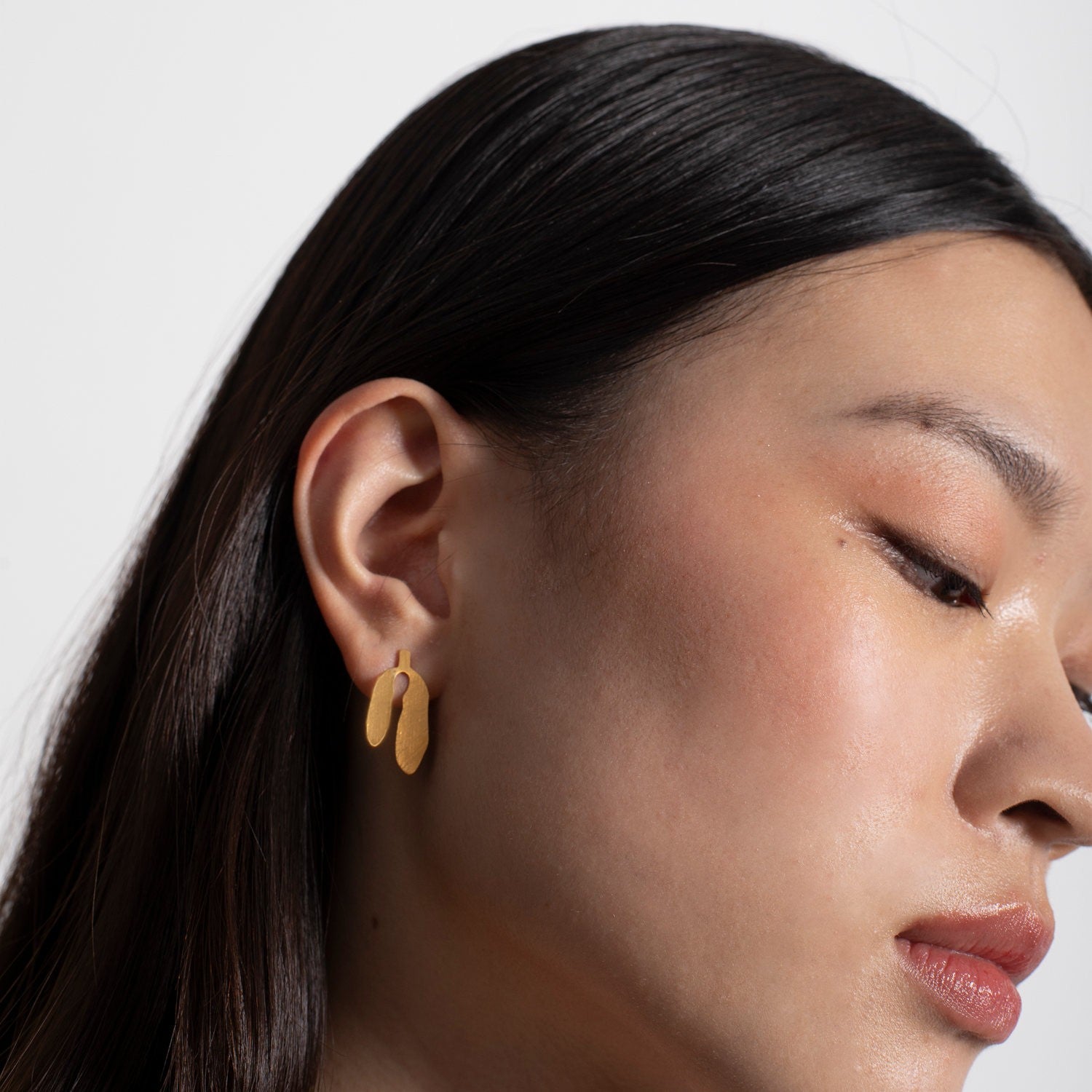 Close-up of a woman wearing gold earrings with a neutral background