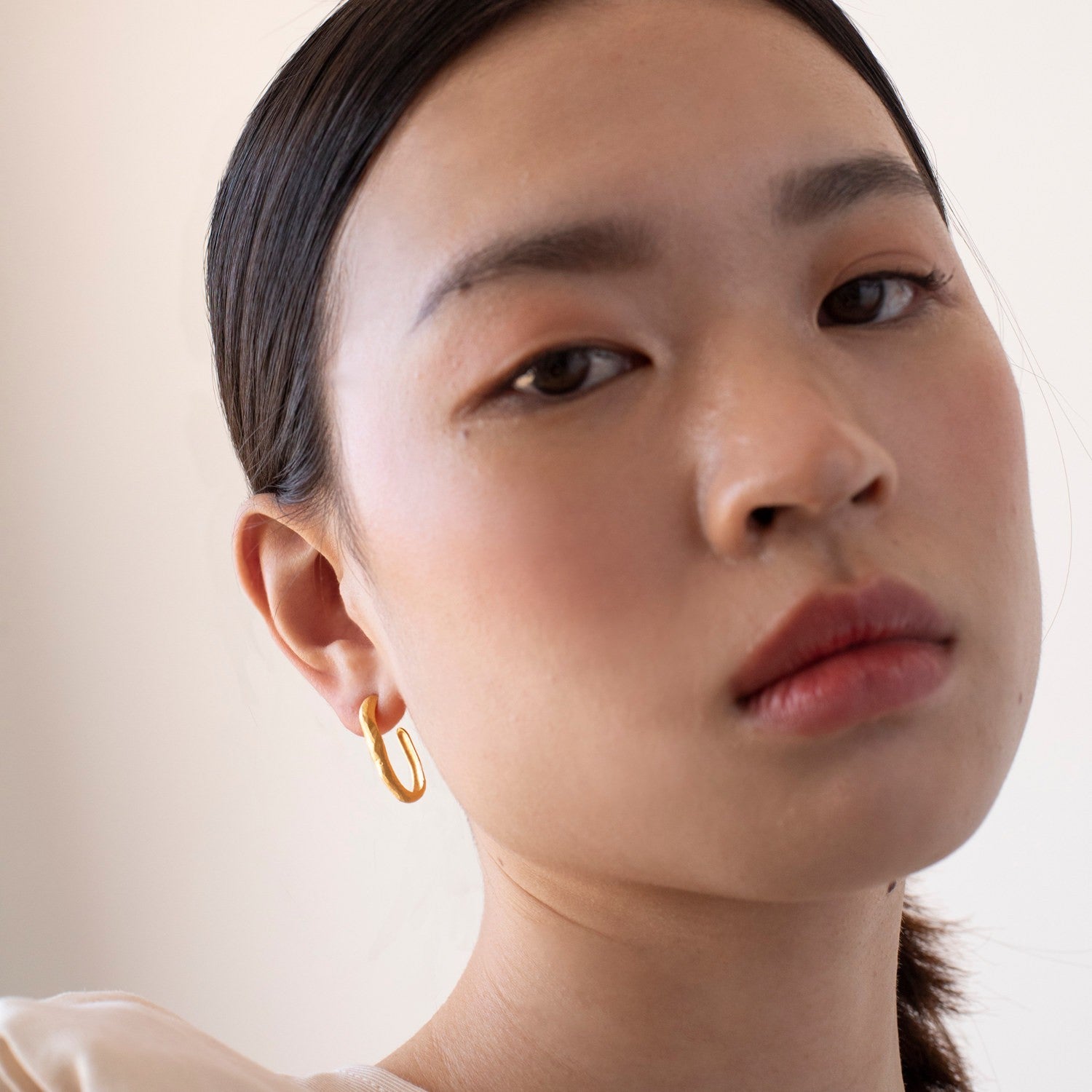 Close-up of a person wearing a gold hoop earring against a neutral background