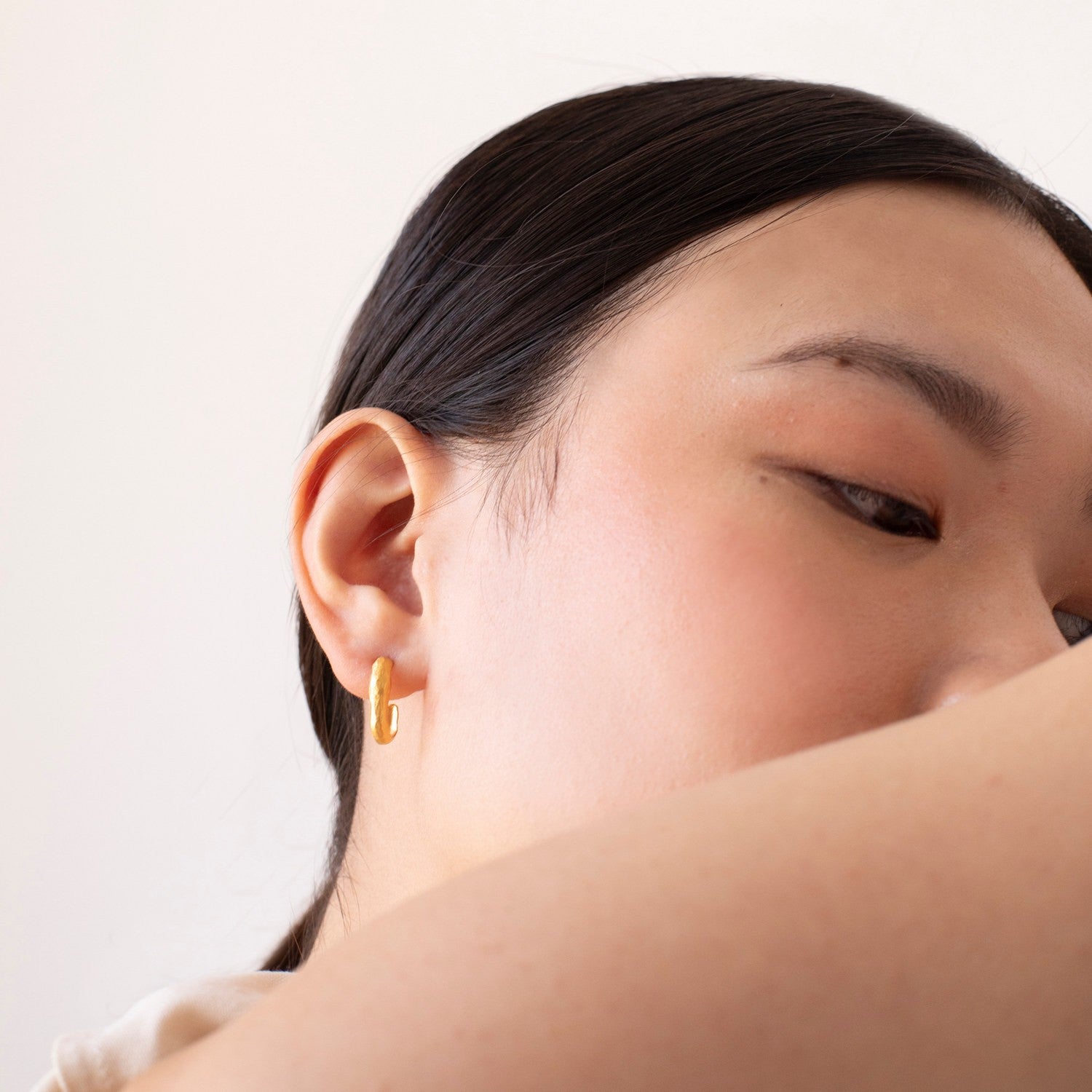 Close-up of a person wearing a gold hoop earring against a neutral background